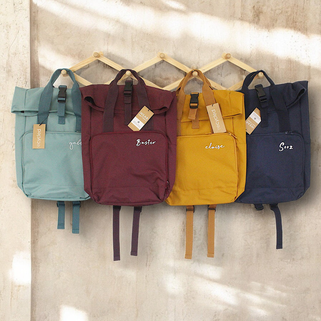 Four colorful backpacks hanging on a wall with visible brand names.