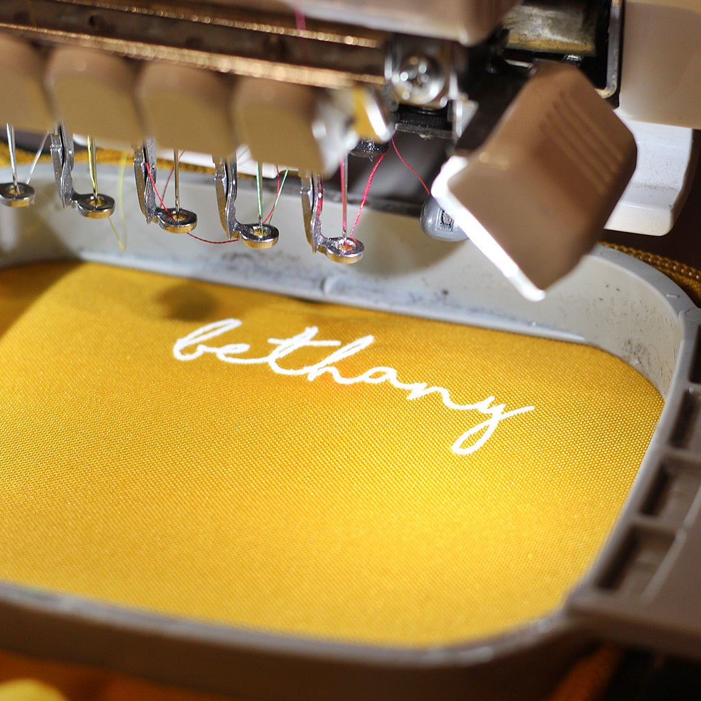 Embroidery machine stitching the name 'bethany' on yellow fabric.