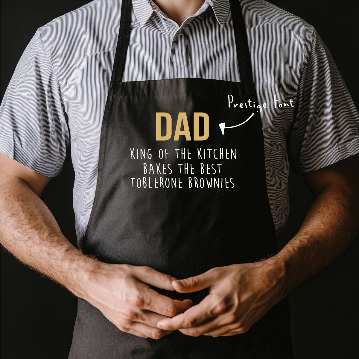 Person wearing a black apron with humorous text design, standing against a dark background.