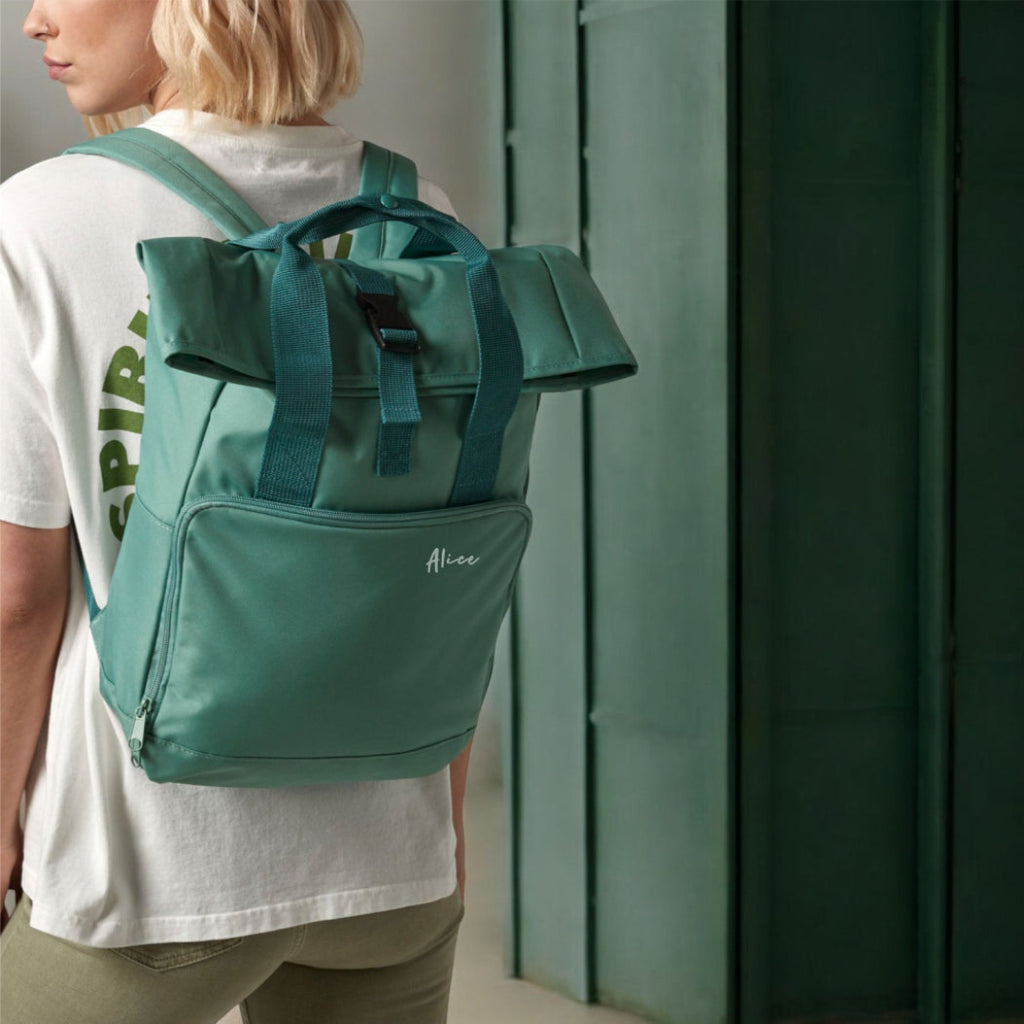 Person wearing a sage backpack with 'Alice' branding against a green wall.