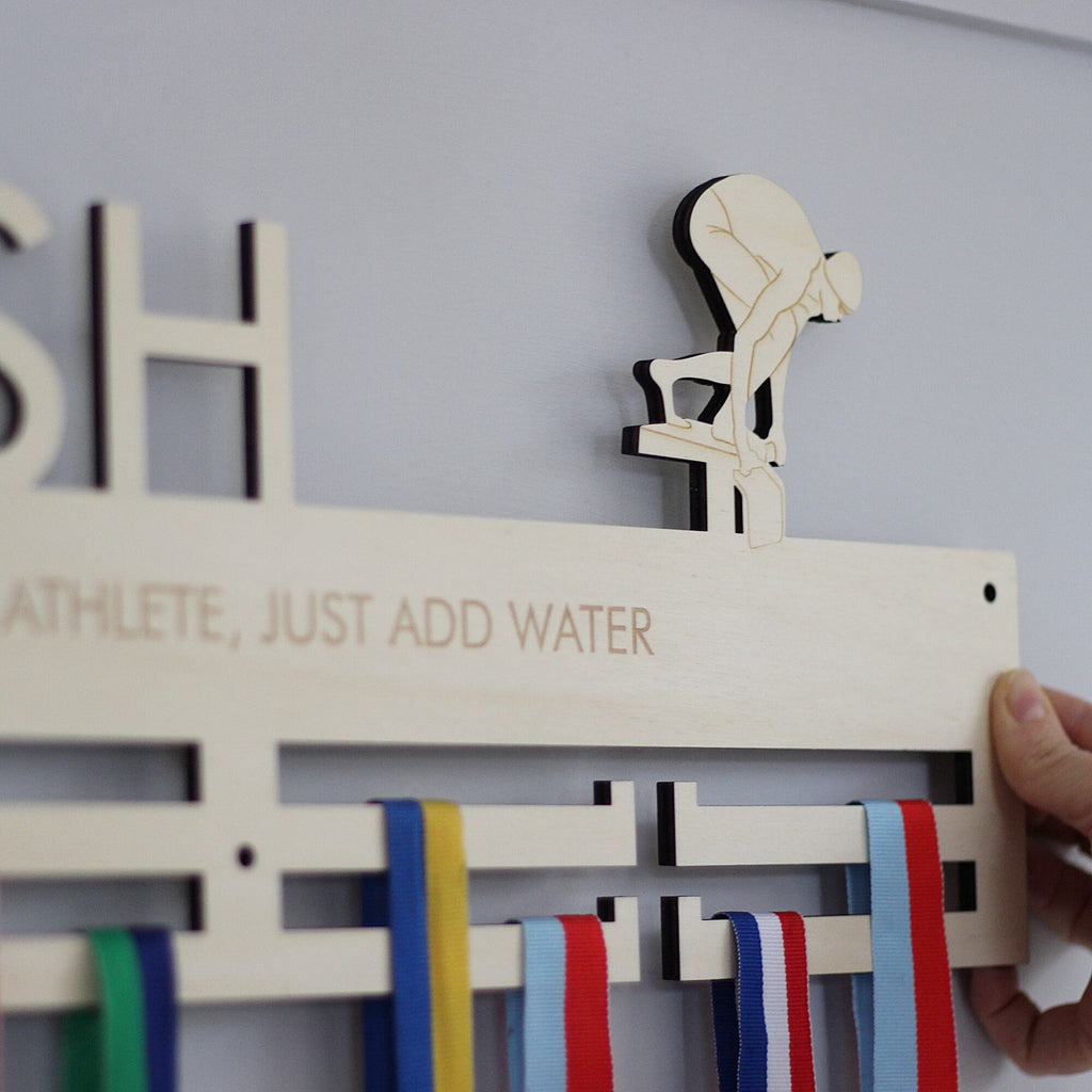 Wooden medal holder with swimmer design and ribbons on a light gray background