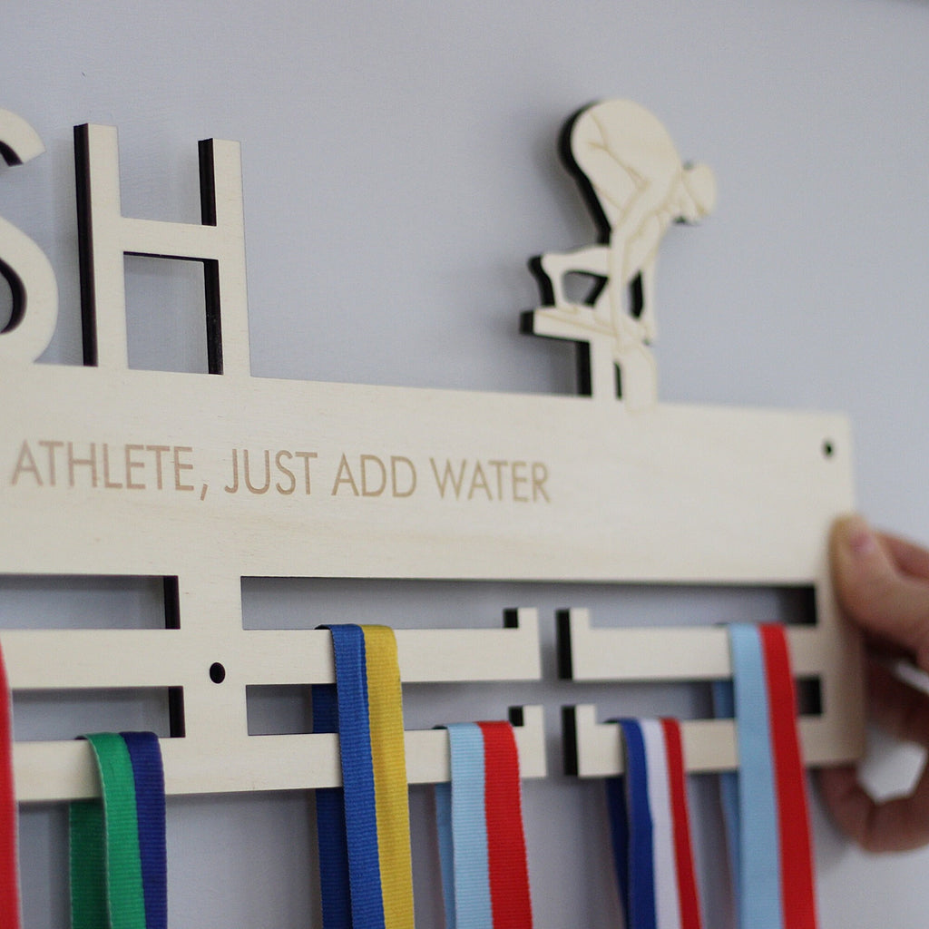 Wooden plaque with ribbons and text 'ATHLETE, JUST ADD WATER' on a plain background