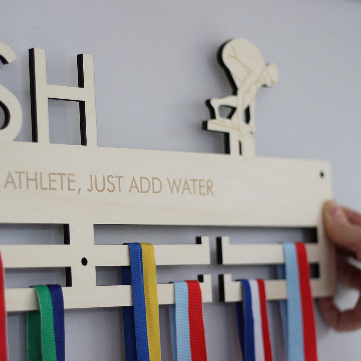 Wooden plaque with ribbons and text 'ATHLETE, JUST ADD WATER' on a plain background