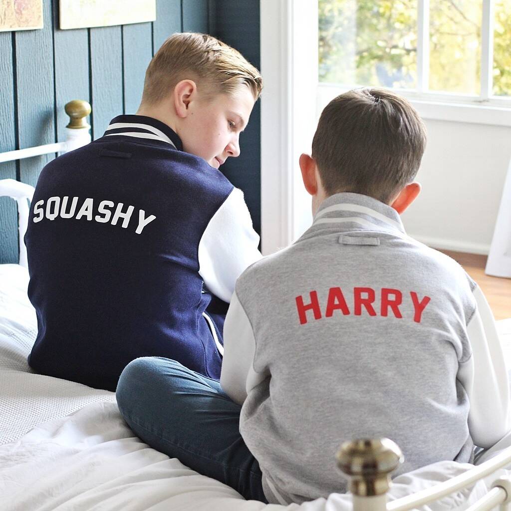 Two children sitting on a bed wearing varsity jackets with 'SQUASHY' and 'HARRY' printed on the back.
