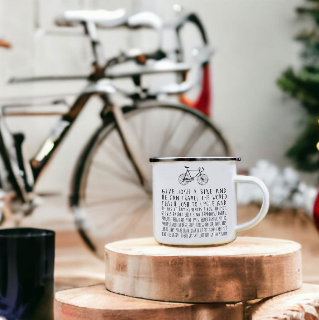 White mug with text and bicycle design on a wooden coaster, with a bicycle in the background.