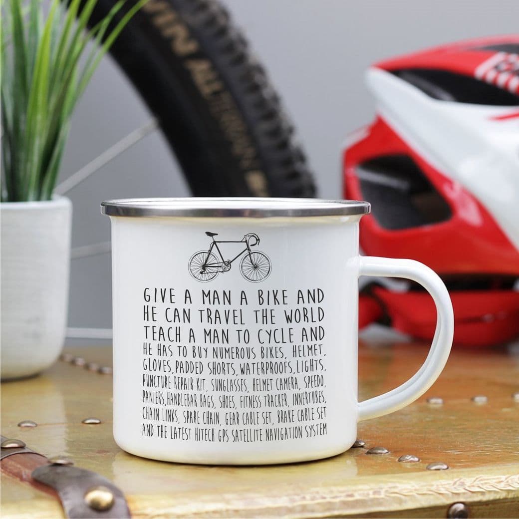 White mug with bicycle-themed text on a wooden surface with a bike and helmet in the background.