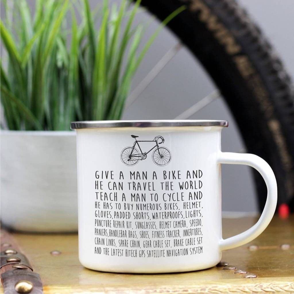White mug with bicycle-themed text on a wooden surface with a plant and bike tire in the background