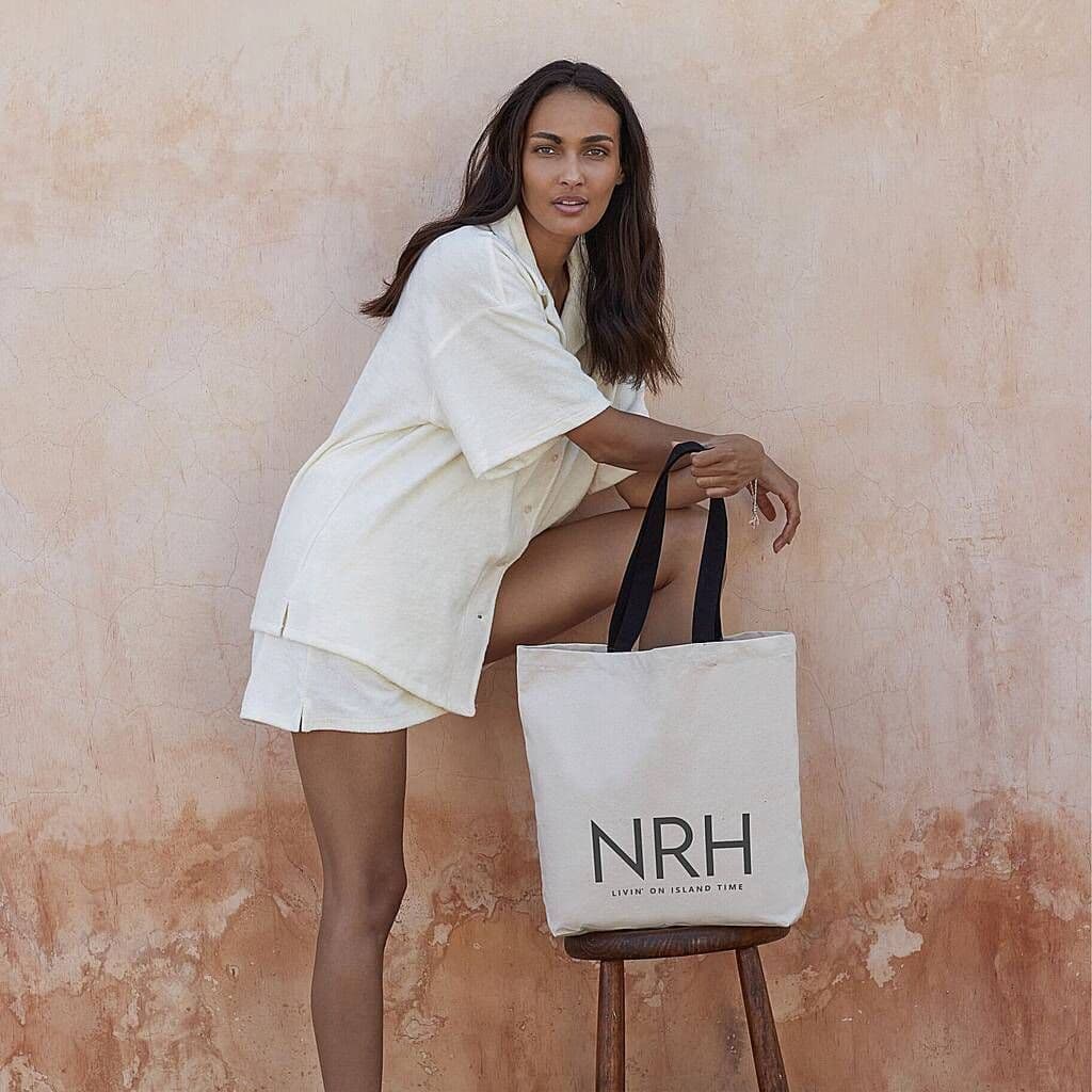 Woman holding a tote bag with 'NRH' branding against a textured wall.
