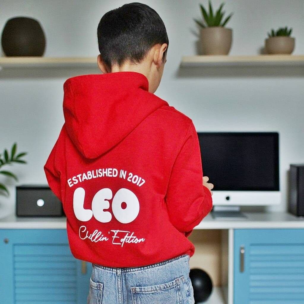 Child wearing a red hoodie with text on the back in a room with shelves and plants.