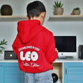 Child wearing a red hoodie with text on the back in a room with shelves and plants.