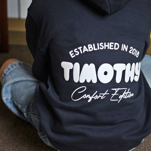 Navy hoodie with white text on the back, worn by a person sitting on the floor.