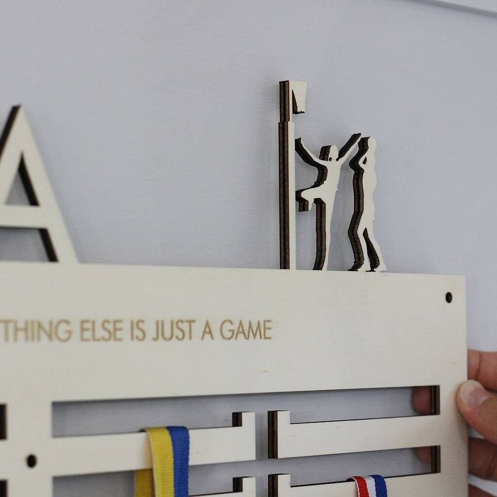 Decorative netball medal hanger  with 'THING ELSE IS JUST A GAME' text and abstract figures on a white background