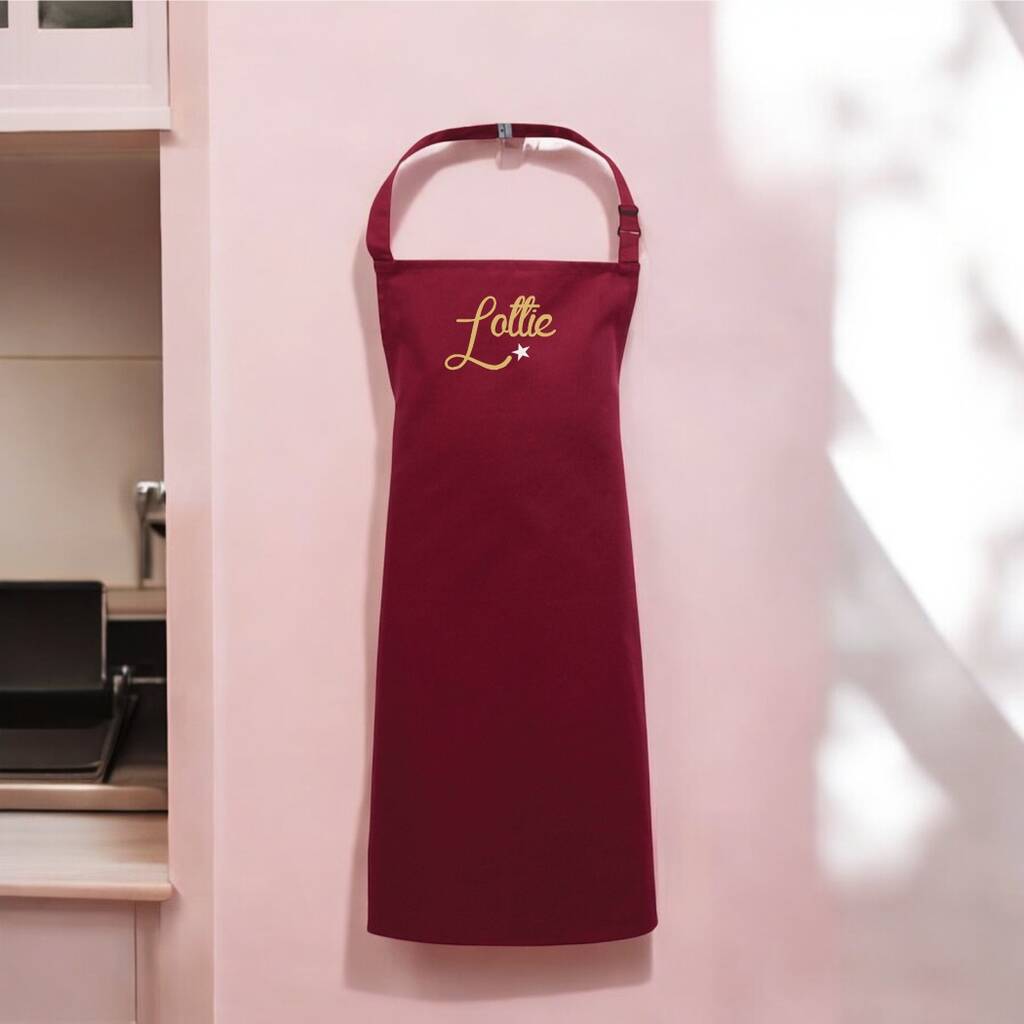 Red apron with 'Lottie' embroidery on a pink wall