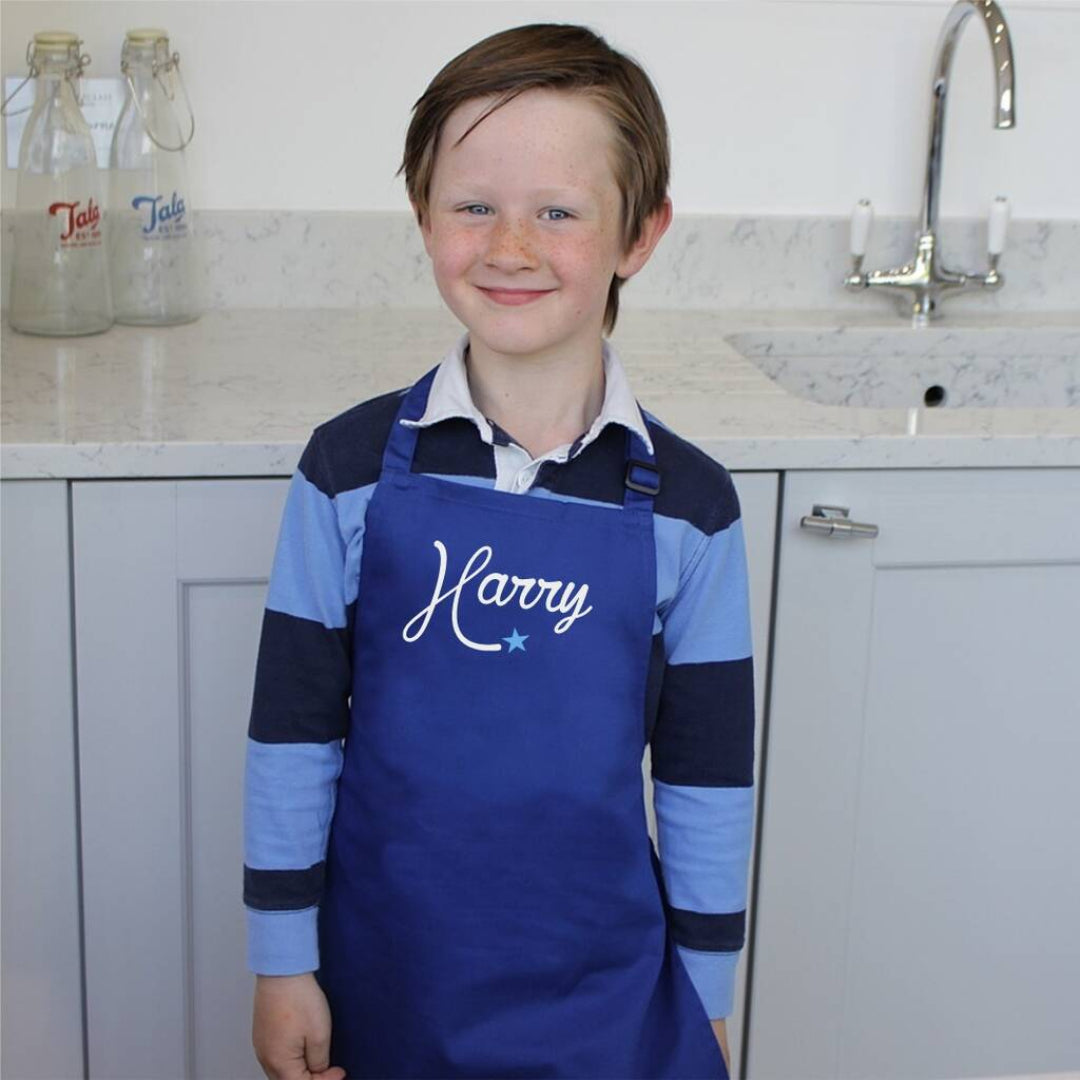 Child wearing a blue apron with 'Harry' written on it in a kitchen.