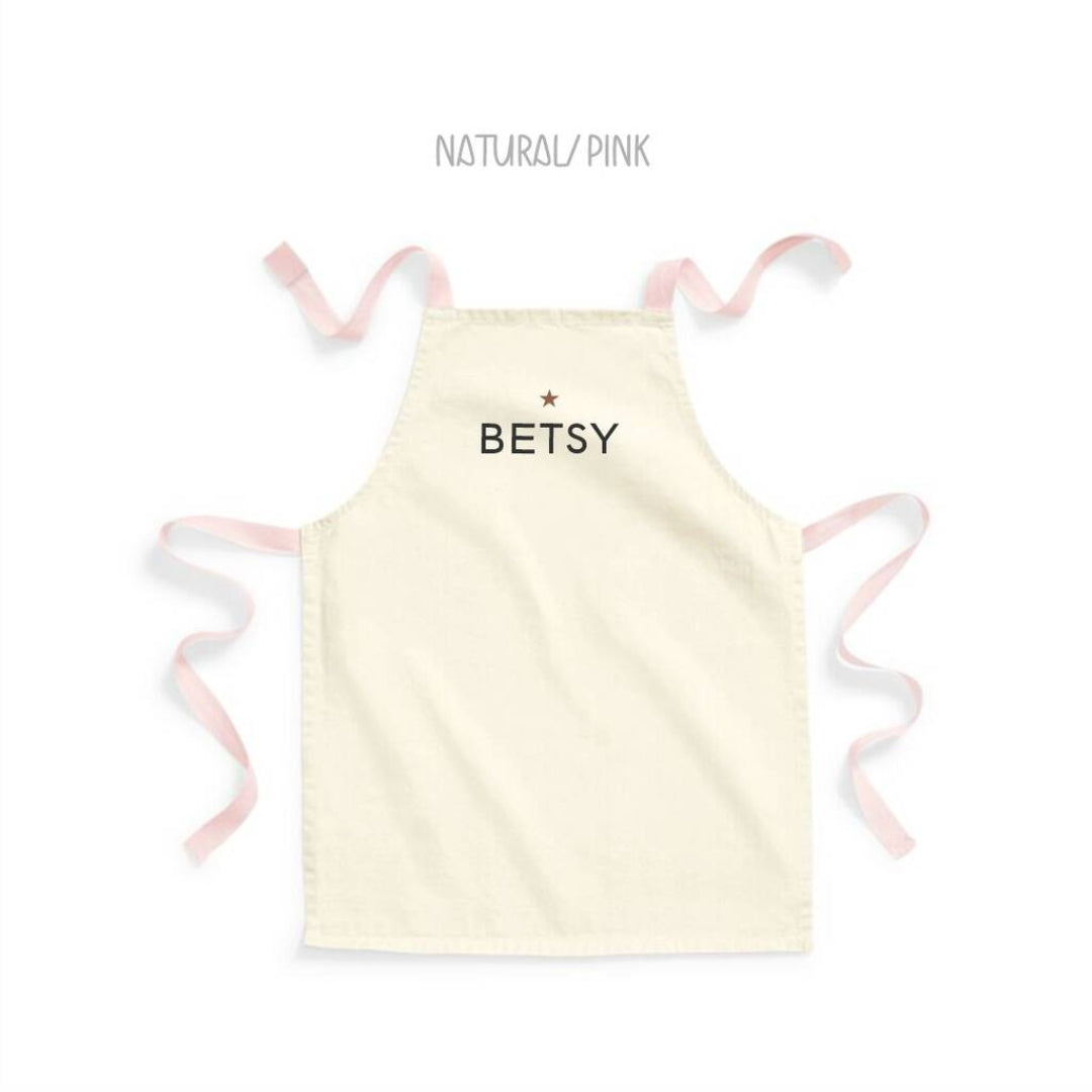 Light yellow apron with 'BETSY' text and pink straps on a white background