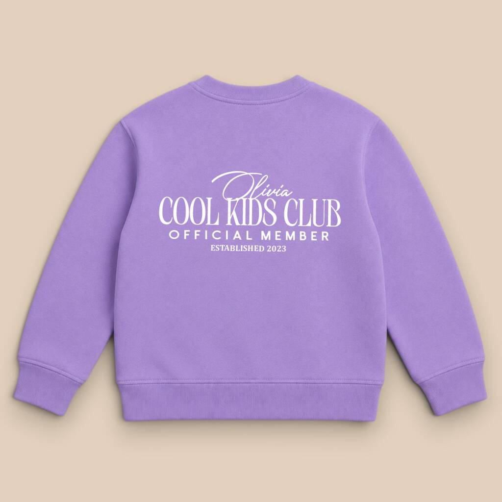 A lavender purple crewneck sweatshirt shown from the back, featuring white printed text that reads 'Olivia COOL KIDS CLUB OFFICIAL MEMBER ESTABLISHED 2023' on a solid beige background.