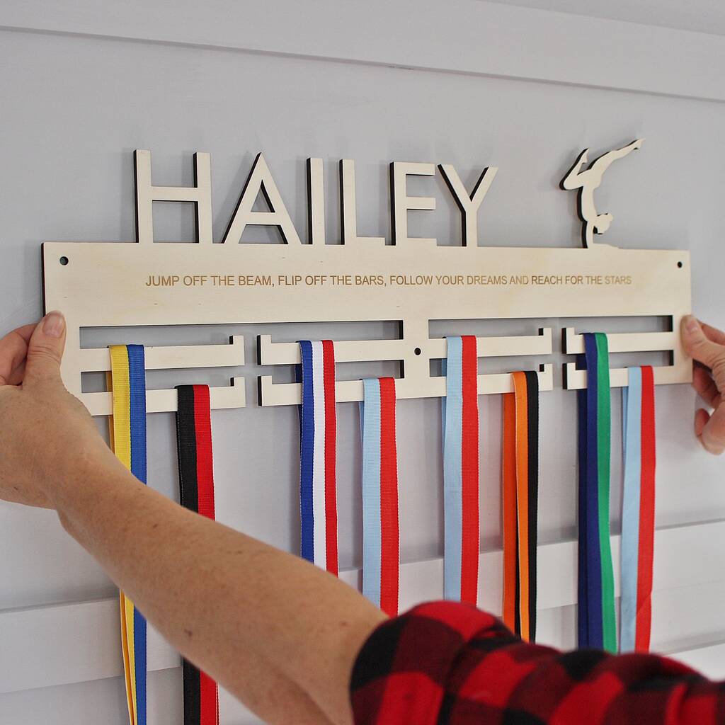 Wooden medal holder with ribbons attached, personalized with 'HAILEY' and motivational text.