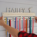 Wooden medal holder with ribbons attached, personalized with 'HAILEY' and motivational text.