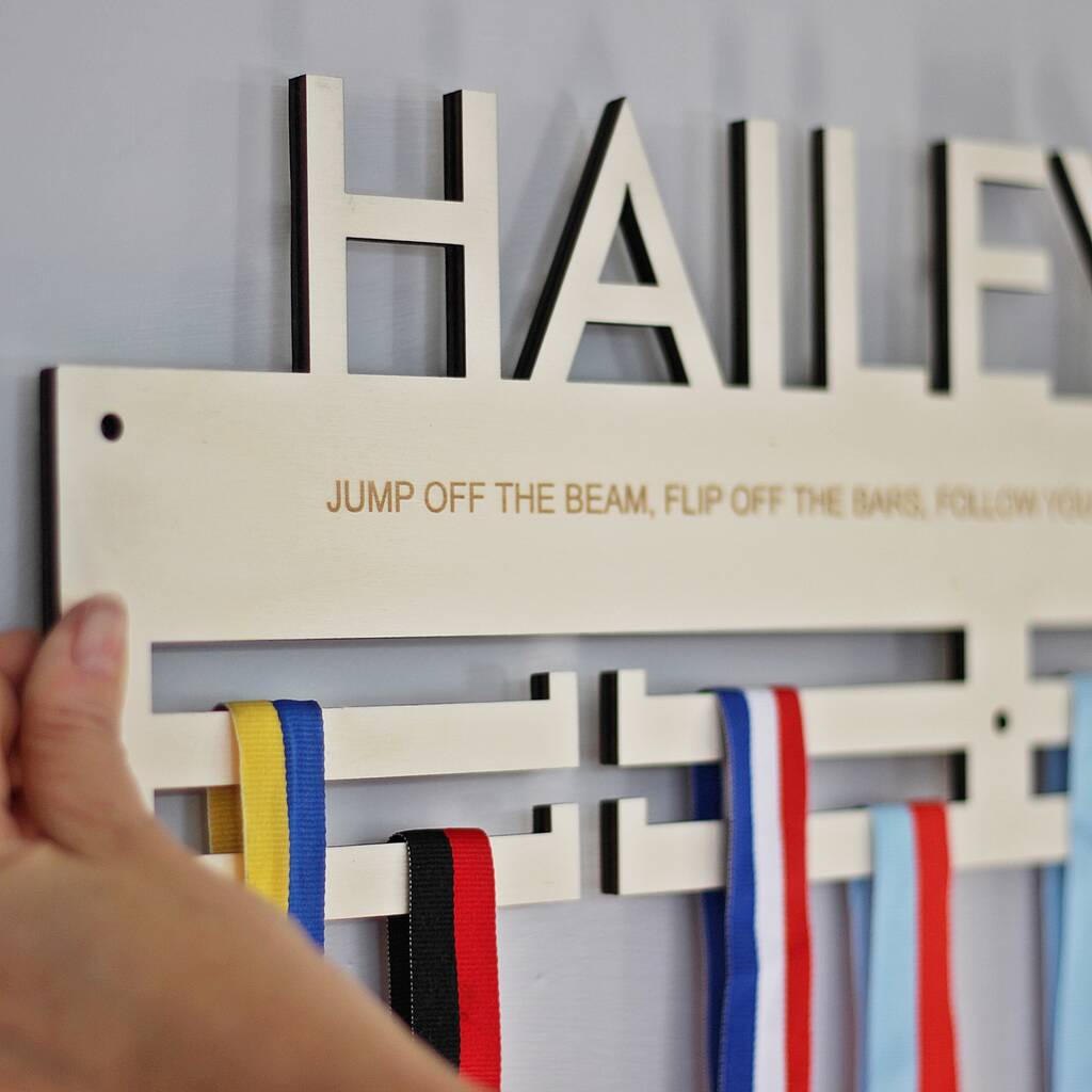 Wooden medal holder with ribbons and 'HAILEY' above on a gray background