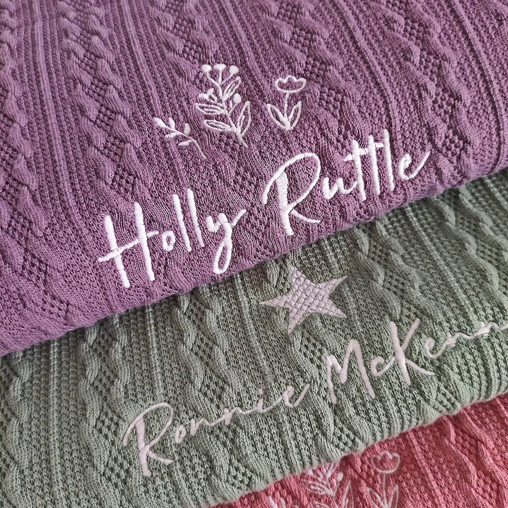 Stack of textured fabric blankets with embroidered names and designs.