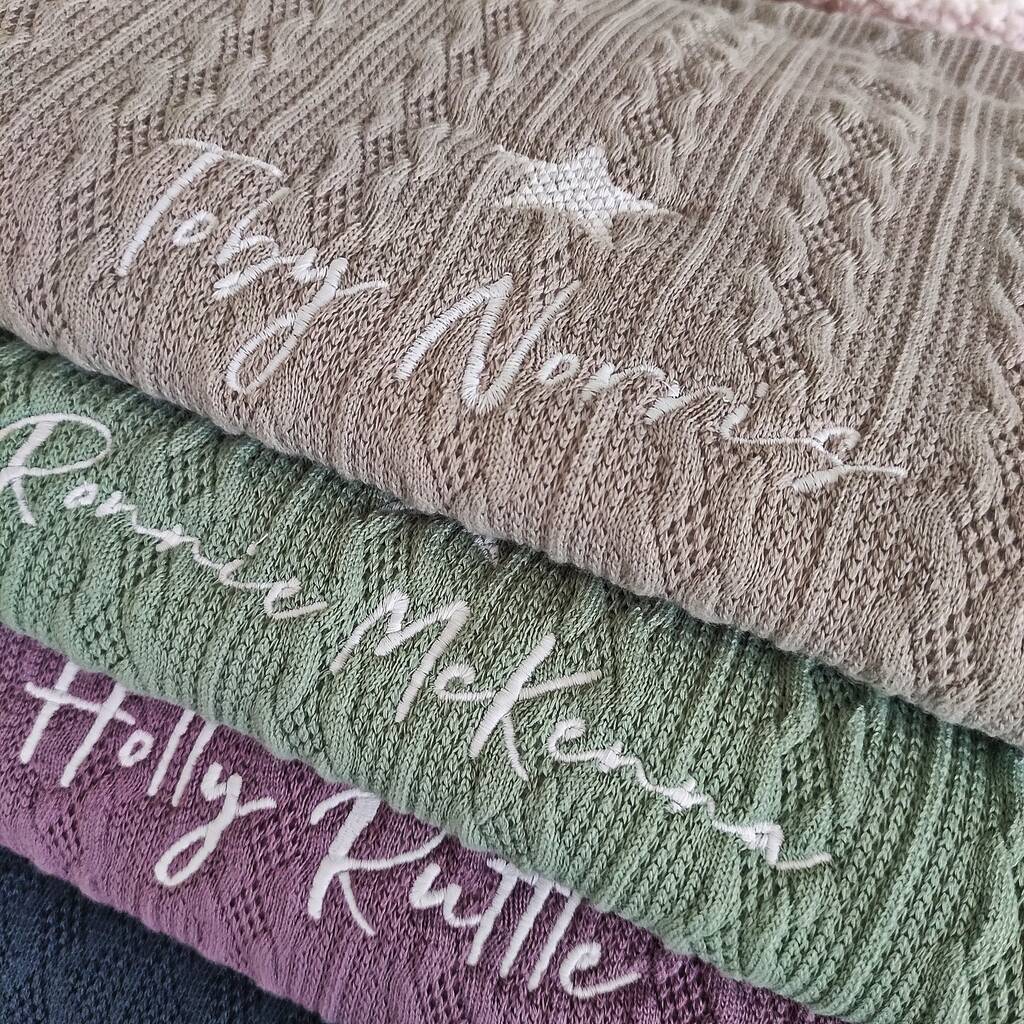 Stack of knitted sweaters with embroidered names on a textured surface
