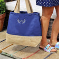 Blue tote bag with beige bottom section held by a person wearing a polka dot dress and sandals.