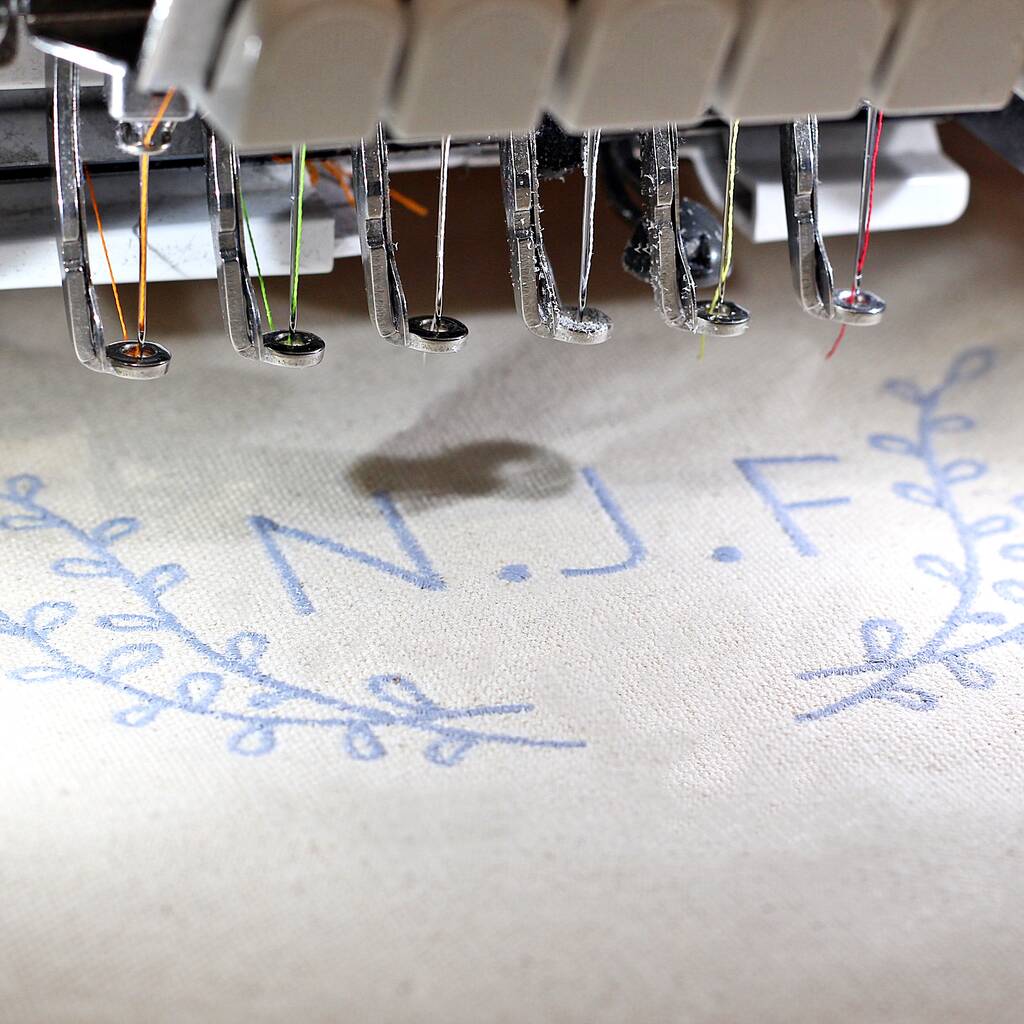 Embroidery machine needle with thread on fabric displaying 'N.J.F.'