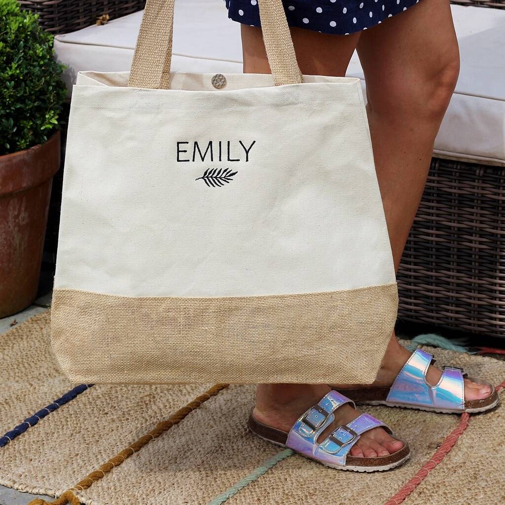 Beige tote bag with 'EMILY' printed on it held by a person wearing sandals.