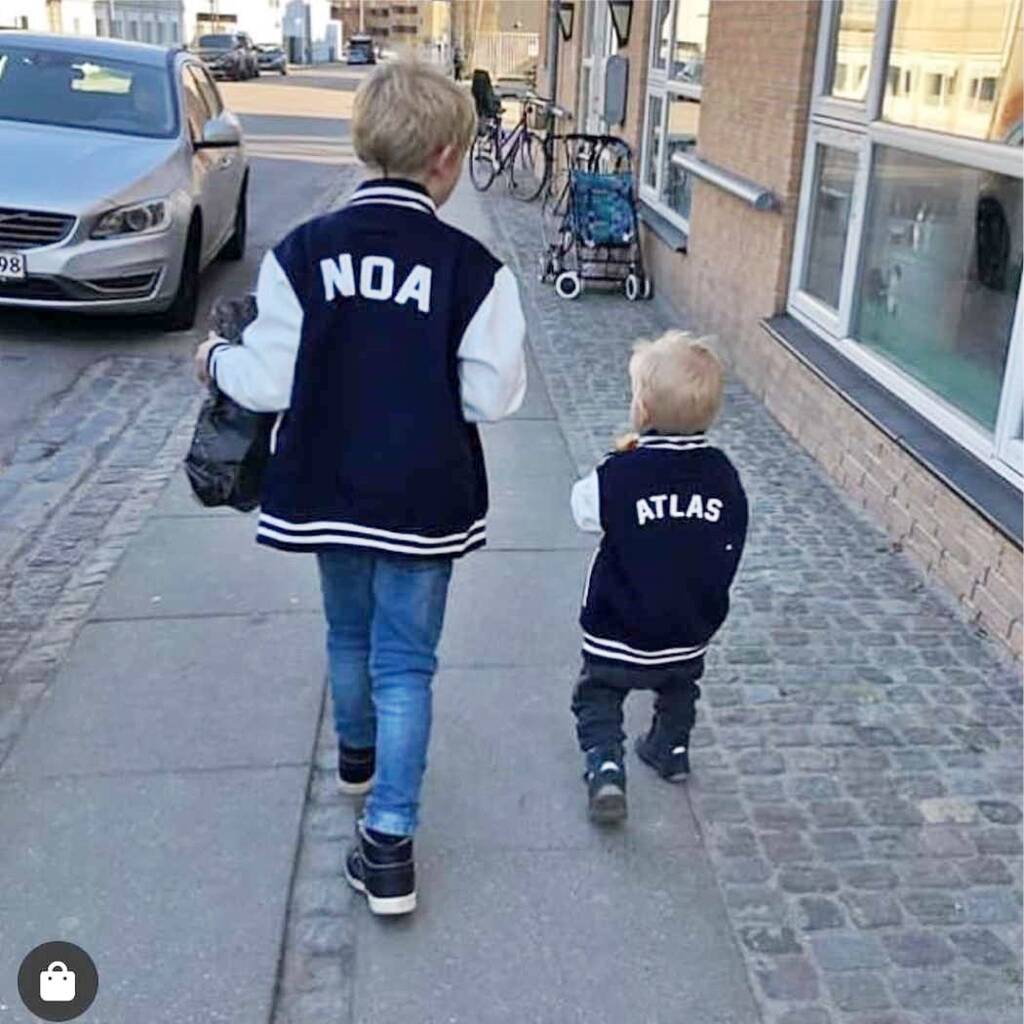 Two children wearing letterman jackets with 'NOA' and 'ATLAS' on a sidewalk.