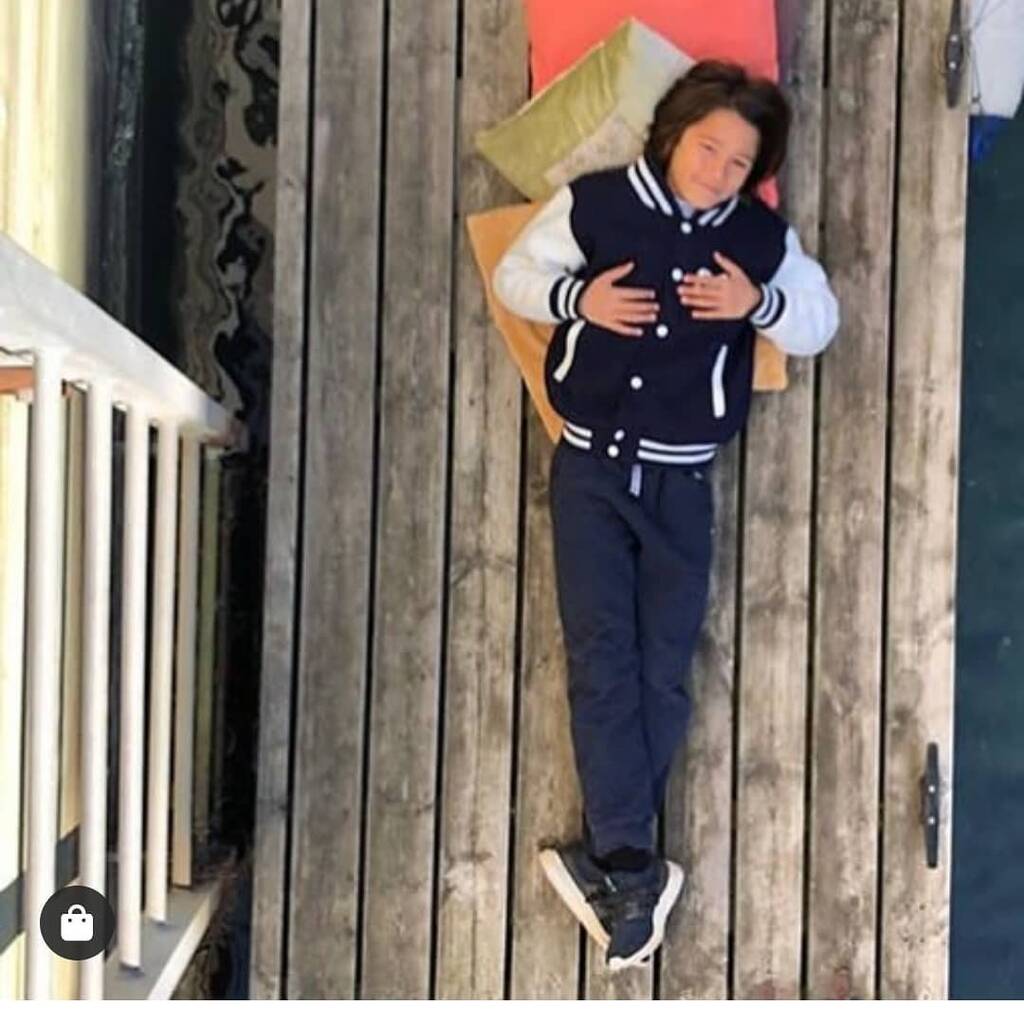 Child wearing a navy varsity jacket and pants lying on a wooden floor.