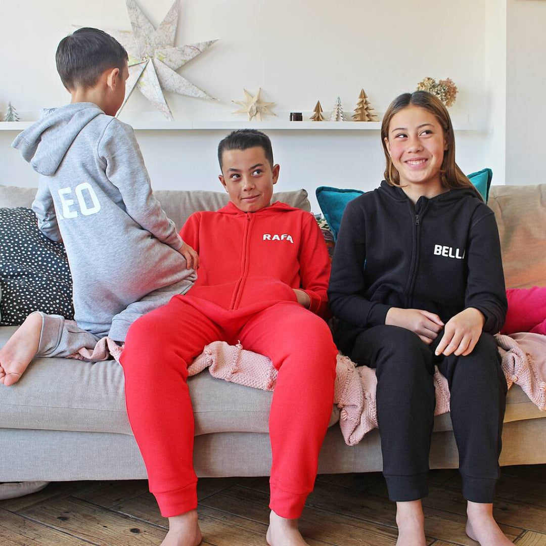 Three children sitting on a couch wearing branded onesies in a living room.