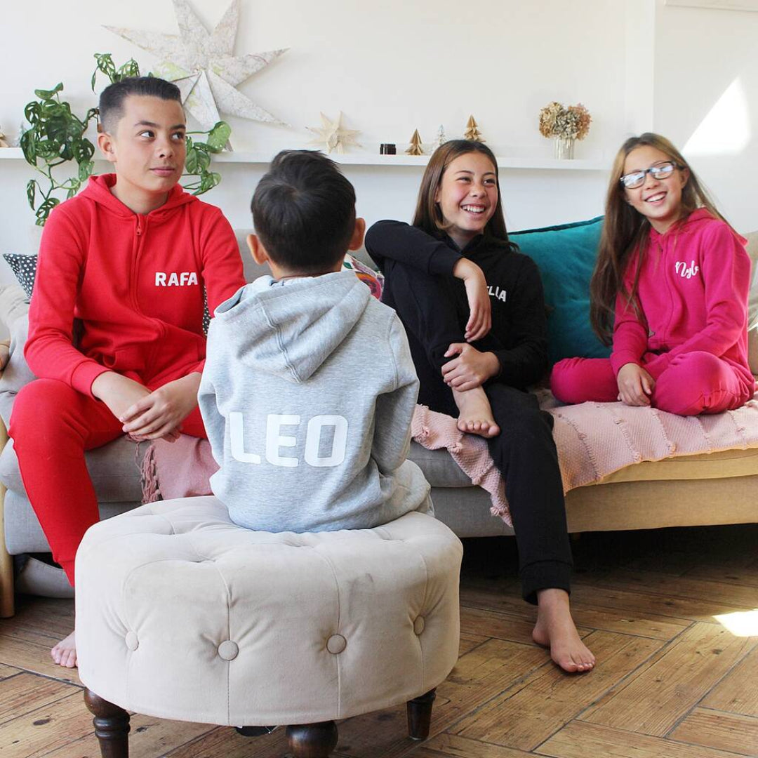 Four people sitting on a couch in a living room, wearing hoodies with names printed on them.