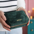 Green velvet pouch with 'MUM' embroidery held by a person, blurred background
