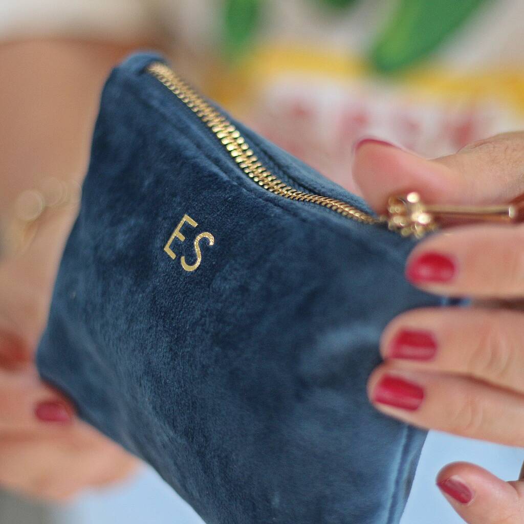 Blue pouch with gold zipper and initials held by a person with red nail polish.