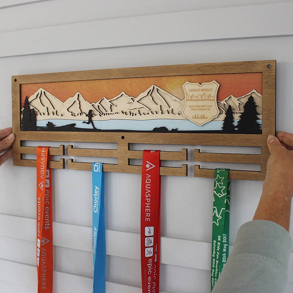 Wooden medal holder with mountain design holding swim caps against a white wall