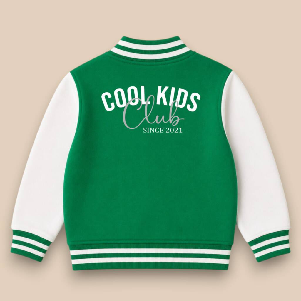 A green and white varsity jacket shown from the back, featuring 'COOL KIDS Club SINCE 2021' printed in white. The jacket has a green body, white sleeves, and green and white striped ribbed collar, cuffs, and hem, set against a solid beige background.