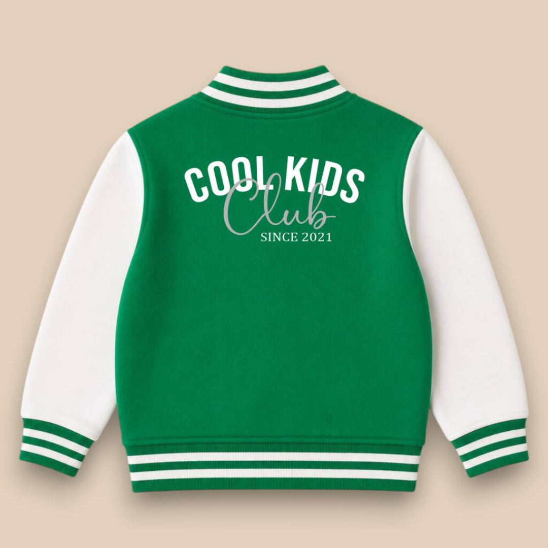 A green and white varsity jacket shown from the back, featuring 'COOL KIDS Club SINCE 2021' printed in white. The jacket has a green body, white sleeves, and green and white striped ribbed collar, cuffs, and hem, set against a solid beige background.