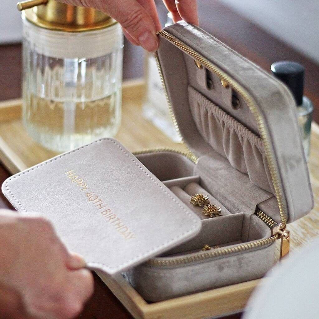 Gray jewelry case with gold interior, containing a ring, on a wooden tray with a glass of water and a black container in the background.