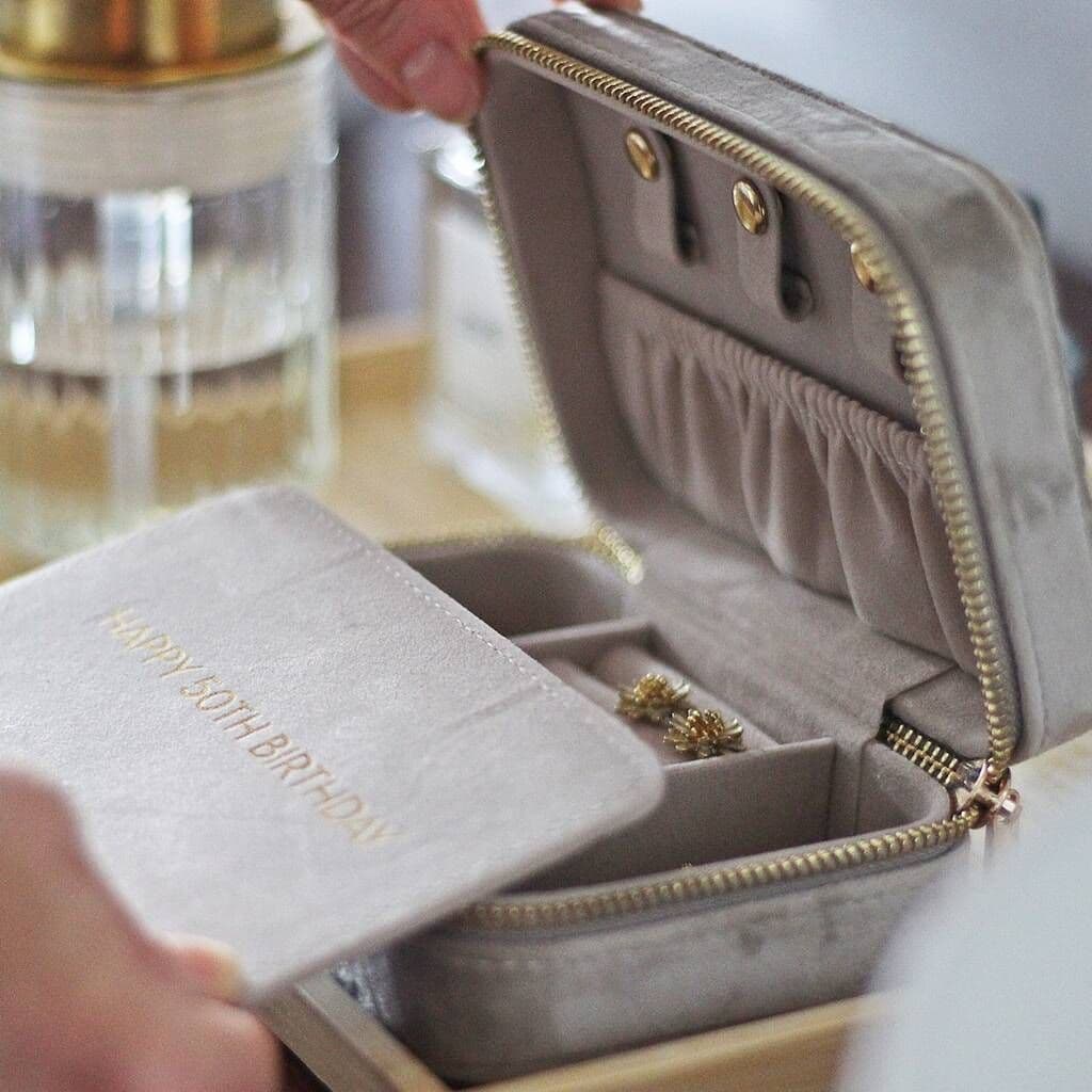 Open jewelry box with gold zipper and earrings inside, on a blurred background.