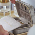 Open jewelry box with gold zipper and earrings inside, on a blurred background.