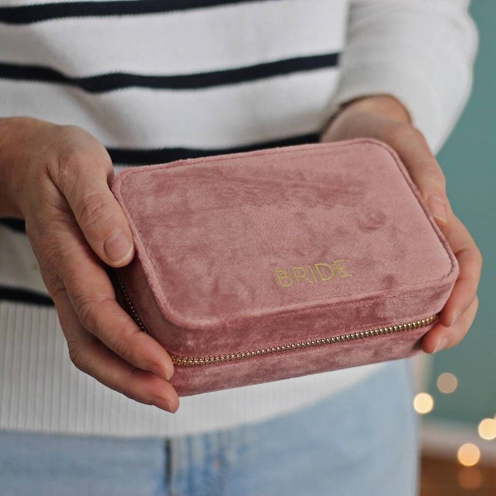 Pink velvet jewelry box with 'BRIDE' embroidery held by a person.