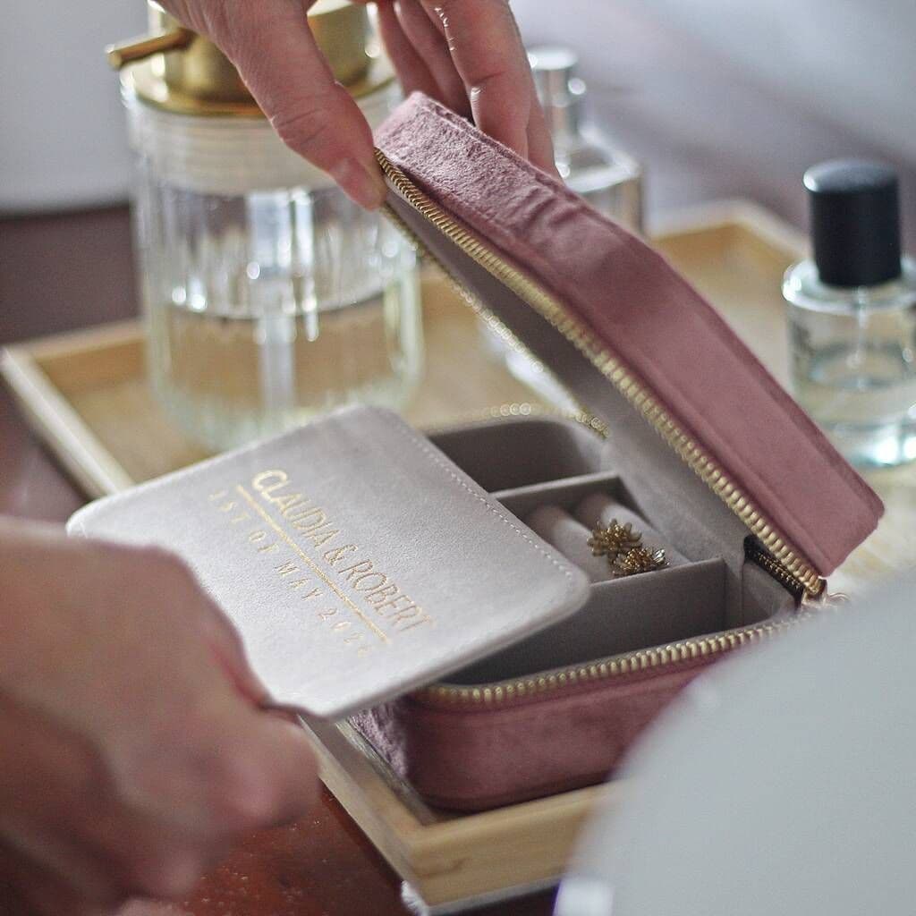 Pink jewelry box with a gold zipper being opened on a table with perfume bottles in the background.