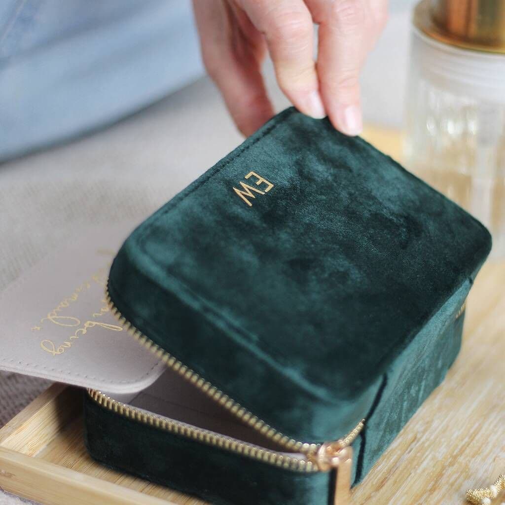 Green velvet jewelry box with gold zipper on a wooden surface