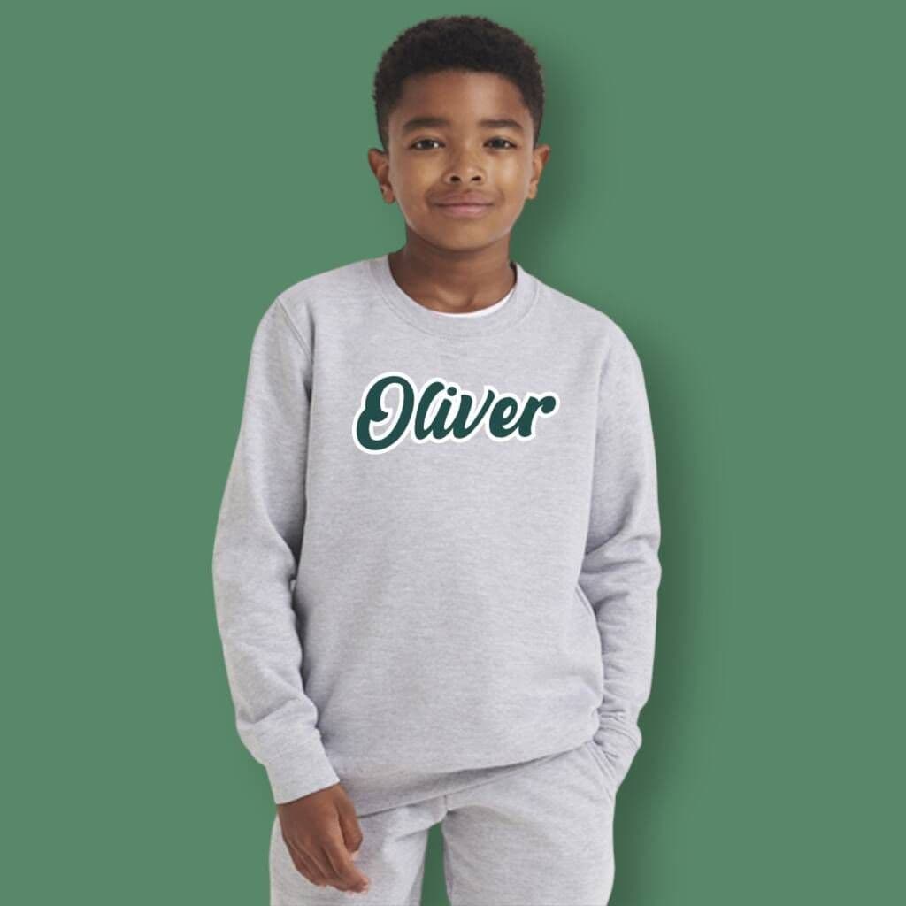 Child wearing a gray sweatshirt with 'Oliver' on a green background