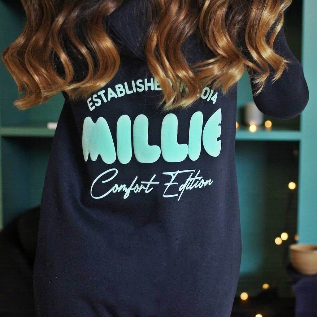 Navy onesie with 'MILLIE Comfort Edition' text on a blurred indoor background