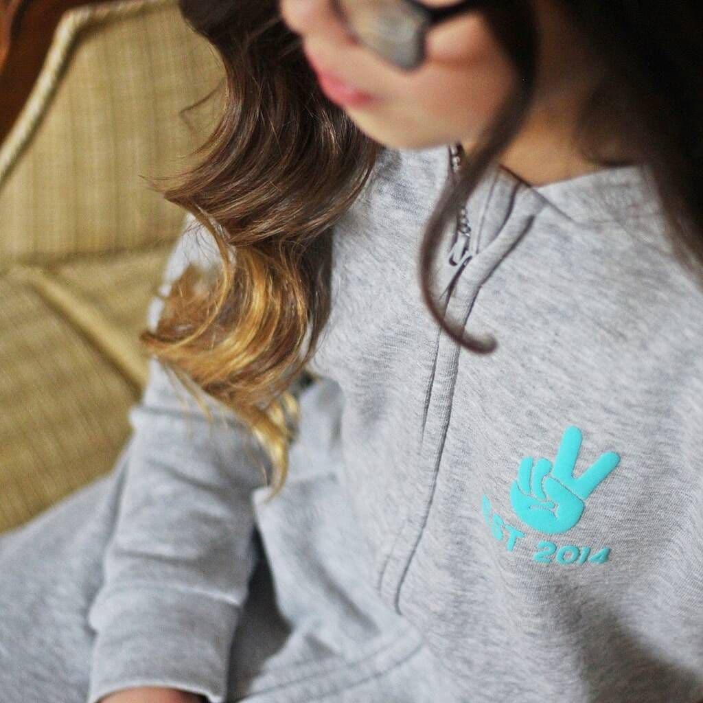 Person wearing a gray onesie with a blue logo on a beige couch