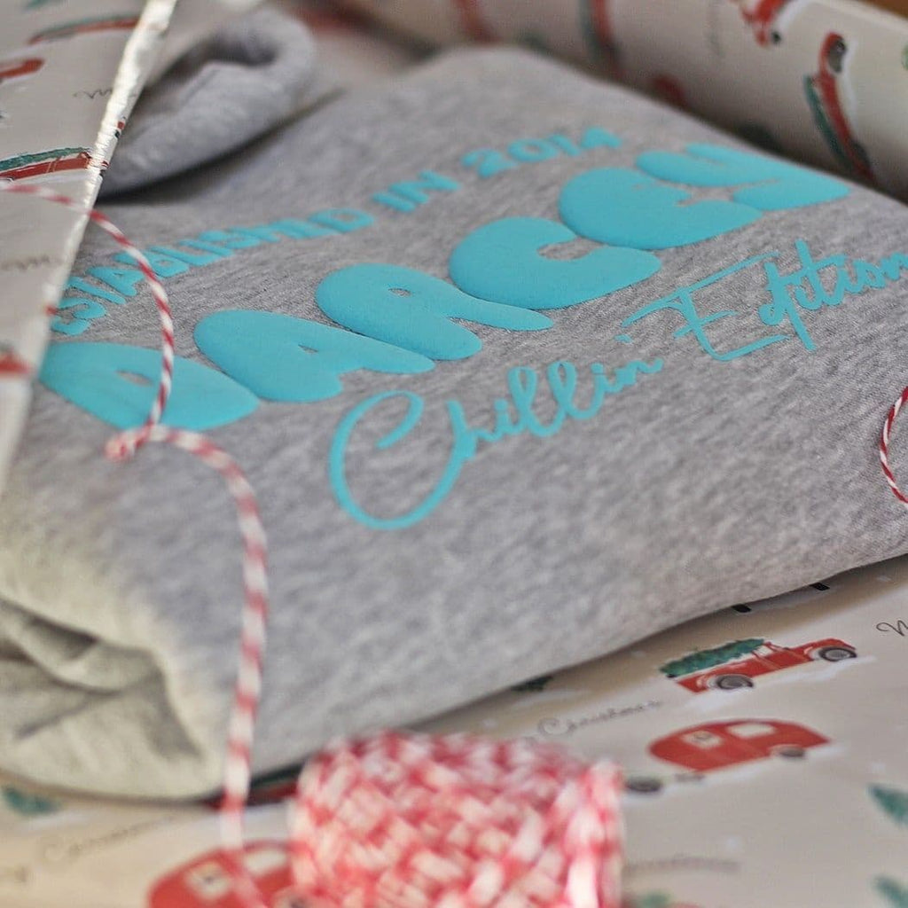 Grey Onesie with turquoise text on a patterned surface