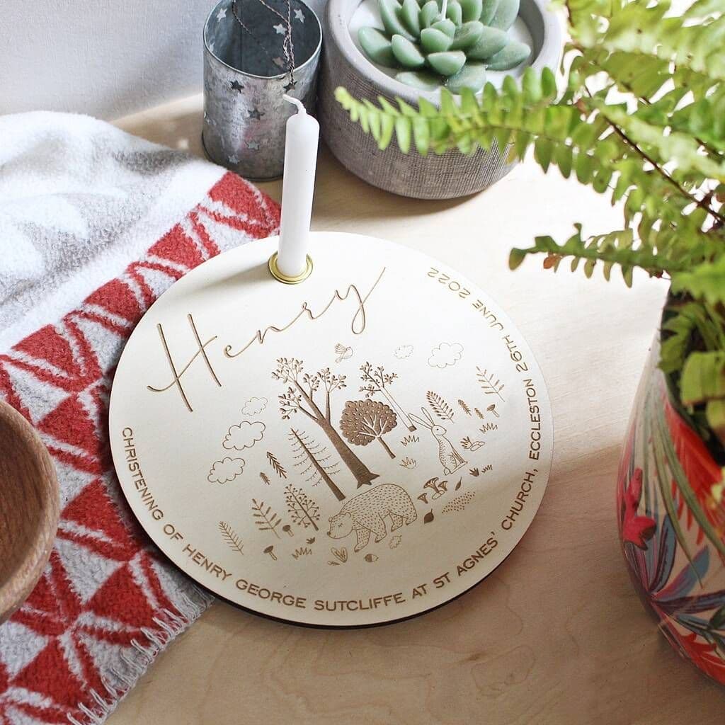 Decorative plaque with 'Henry' engraved, surrounded by plants and a candle on a wooden surface.