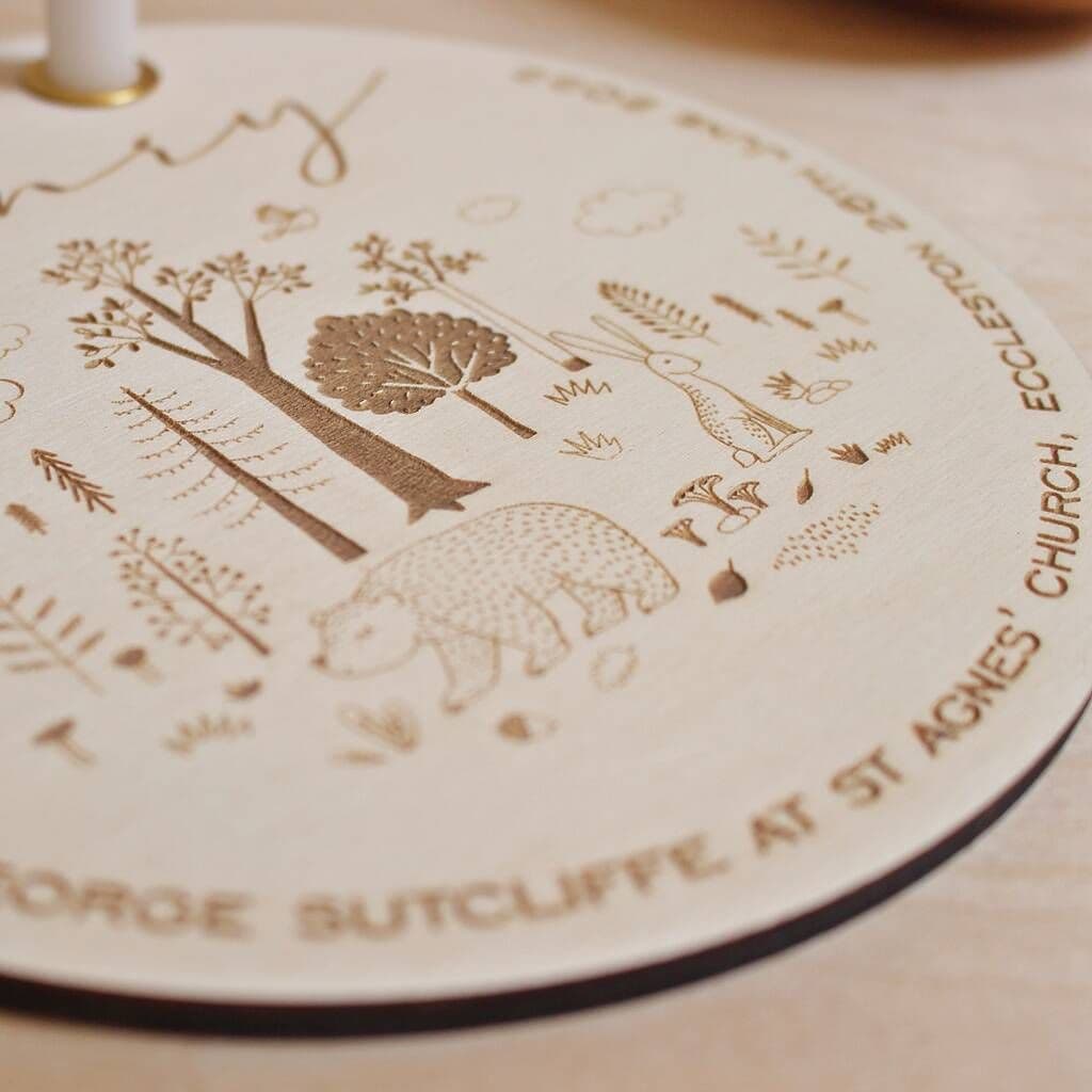 Round wooden coaster with engraved nature-themed design and text on a wooden surface.