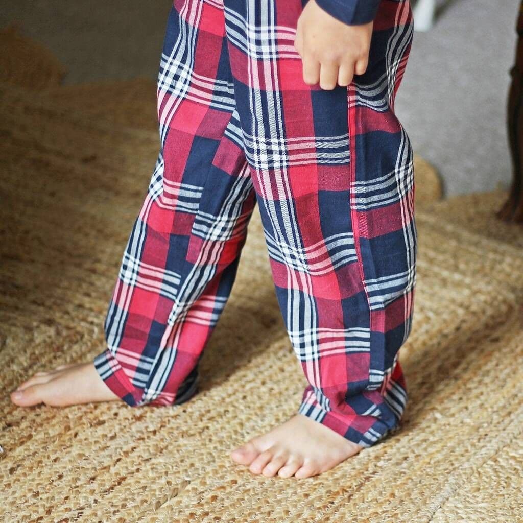 Child wearing red and blue plaid pajama pants on a textured floor.